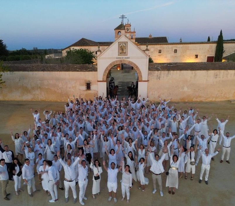 Grupo de personas vestidas de blanco y saludando a la camara a las puertas de la Hacienda la soledad en Sevilla